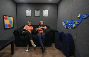 Sensory Explorers Comfort Station at Akron Zoo featuring tactile gear-shaped wall activities and blue cushioned seating.